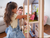 Father and young girl placing a doll inside a premium wood-framed dollhouse with exposed natural wood construction