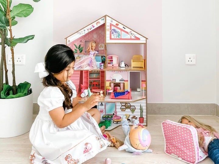 Girl playing with dolls in front of dollhouse